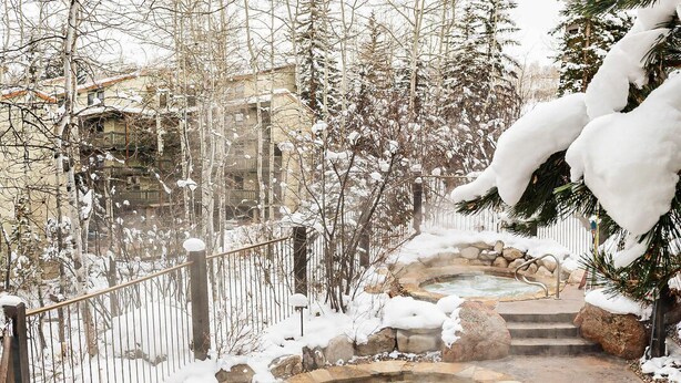 A hot spring area with stone-tiled edges, surrounded by snow-covered trees and a metal fence.
