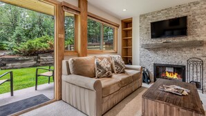 A cozy living room with a fireplace, a sofa with cushions, a coffee table, and a TV mounted on a brick wall. - 🏔️Ski-In, Ski-Out~Hot Tub~Studio Premier 301🏔️ (Snowmass Village)