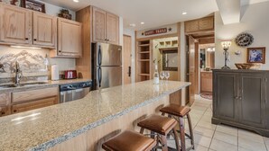 A kitchen with wooden cabinets, a granite countertop, and bar stools. - 🏔️Ski Access~Hot Tub~Studio Premier 305🏔️ (Snowmass Village)