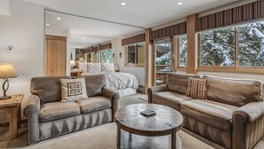 Un salón moderno con sofás de cuero, una mesa de centro redonda y amplios ventanales con vistas a árboles cubiertos de nieve.