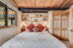 Ein Schlafzimmer mit einem großen Bett, Holzboden, Regalen mit Dekoration und einem Fenster.