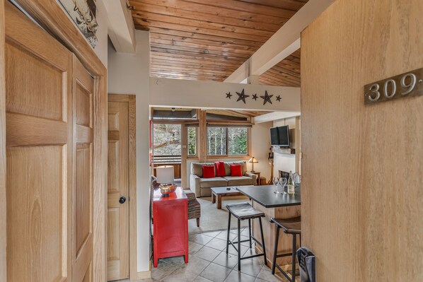 A cozy interior with a wooden ceiling, a kitchen area, a living room with a sofa and red cushions, and a dining area with stools. - 🏔️Ski Access~Hot Tub~Top Floor~Studio Premier 309🏔️ (Snowmass Village)
