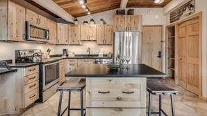 Een keuken met houten kastjes, een centraal eiland met krukken, roestvrijstalen apparatuur en een houten plafond.