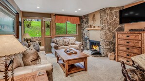 A cozy living room with a fireplace, leather sofa, wooden coffee table, and a television mounted on the wall.