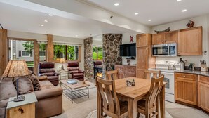 A modern living room with a sofa, coffee table, and fireplace. There is a dining area with a wooden table and chairs. The kitchen features wooden cabinets and a microwave. - 🏔️Slopeside~Hot Tub~Studio Deluxe 408🏔️ (Snowmass Village)