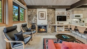 Una sala de estar moderna con chimenea de piedra, sillones de cuero, un sofá rojo y una zona de cocina con armarios blancos y un microondas.