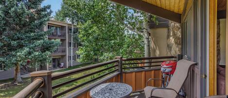 A balcony with a table and chairs, a wooden railing, and a view of neighboring buildings and trees.
