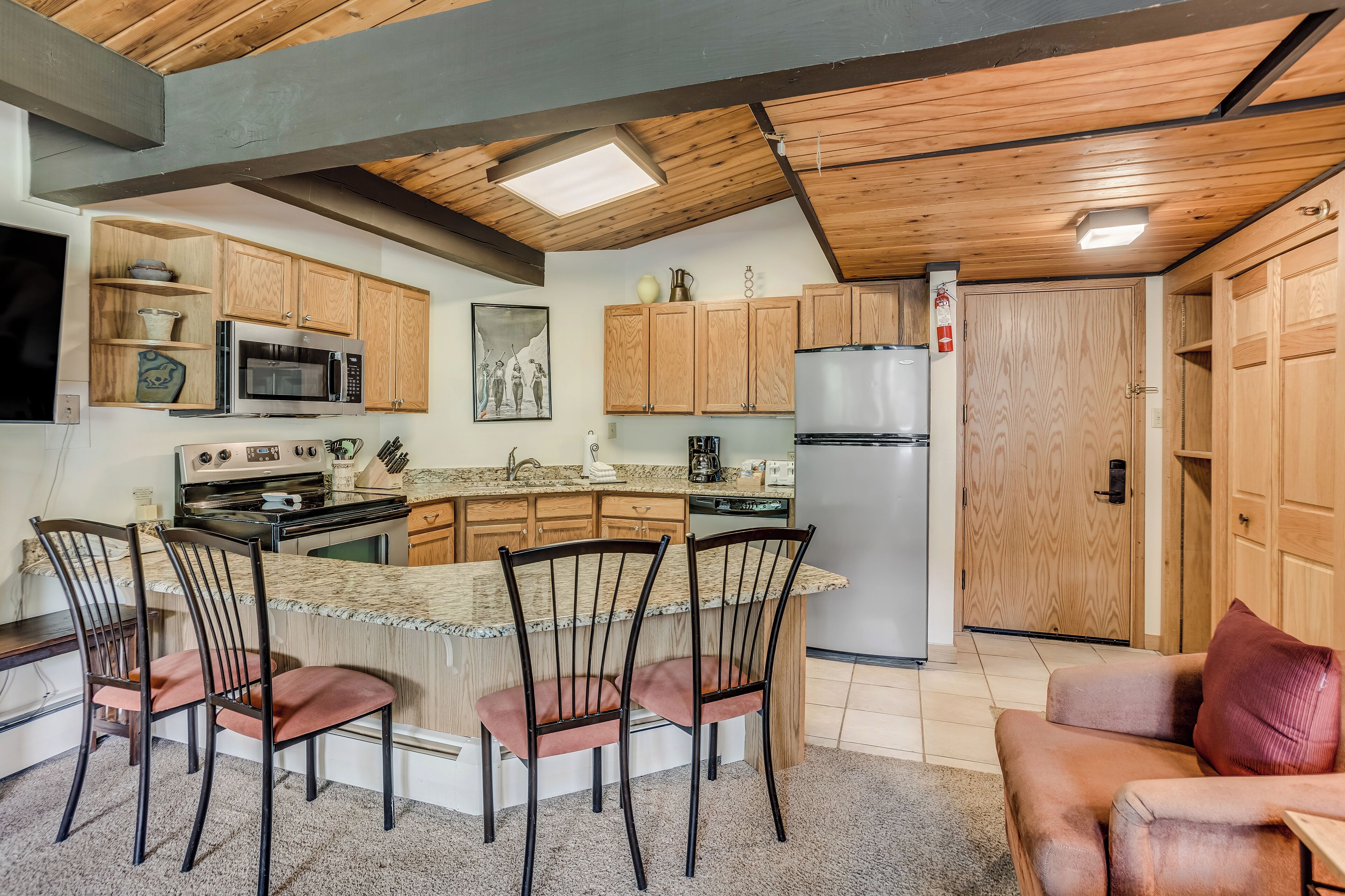 A kitchen with wooden cabinets, a central island with chairs, a refrigerator, and a microwave.