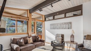 A modern living room with a brown leather sofa, a round coffee table, and two leather armchairs. There is a large window providing natural light and a view of the outside. - 🏔️Slopeside~Hot Tub~Top Floor~Studio Deluxe 414🏔️ (Snowmass Village)