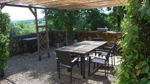 Un patio al aire libre con mesa y sillas, rodeado de muros de piedra y vegetación.