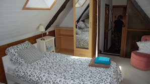 Un dormitorio con techo inclinado, una cama con ropa de cama estampada, un armario de madera, una mesita de noche y un espejo.