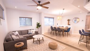 A modern living room with a sofa, coffee table, and ottoman, a dining area with chairs and a table, and a ceiling fan. - 🌵 Cozy Cactus Home near Old Town & ASU 🌵 Pool ⭐ Game Room ⭐ BBQ ⭐ Fire Pit ⭐ (Tempe)