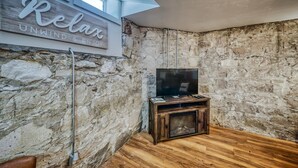 A room with a stone wall, a wooden entertainment unit with a TV, and a sign that reads "Relax Unwind & Enjoy". - The perfect spot in Salida - F Street Hideaway! (Salida)