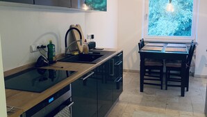 A modern kitchen with dark cabinets, a wooden countertop, and a built-in oven. There's a dining area with a table and chairs, and a window with a view of trees. - Modern vacation apartment "La Fredo" near Lake Starnberg, 5 minutes' walk to public transport (Wolfratshausen)