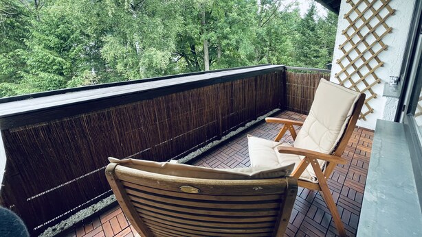 A balcony with a wooden floor, a wicker chair with a cushion, and a lattice wall. - Modern vacation apartment "La Fredo" near Lake Starnberg, 5 minutes' walk to public transport (Wolfratshausen)