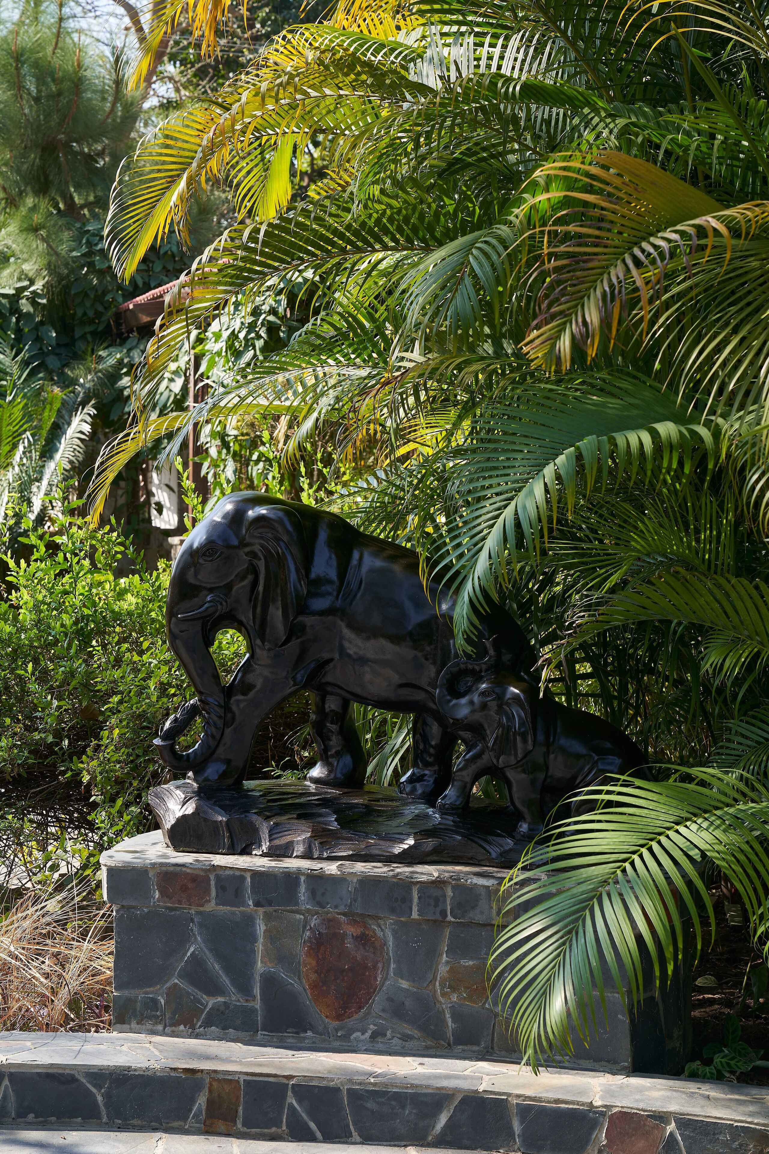 A statue of an elephant on a stone pedestal surrounded by lush greenery.