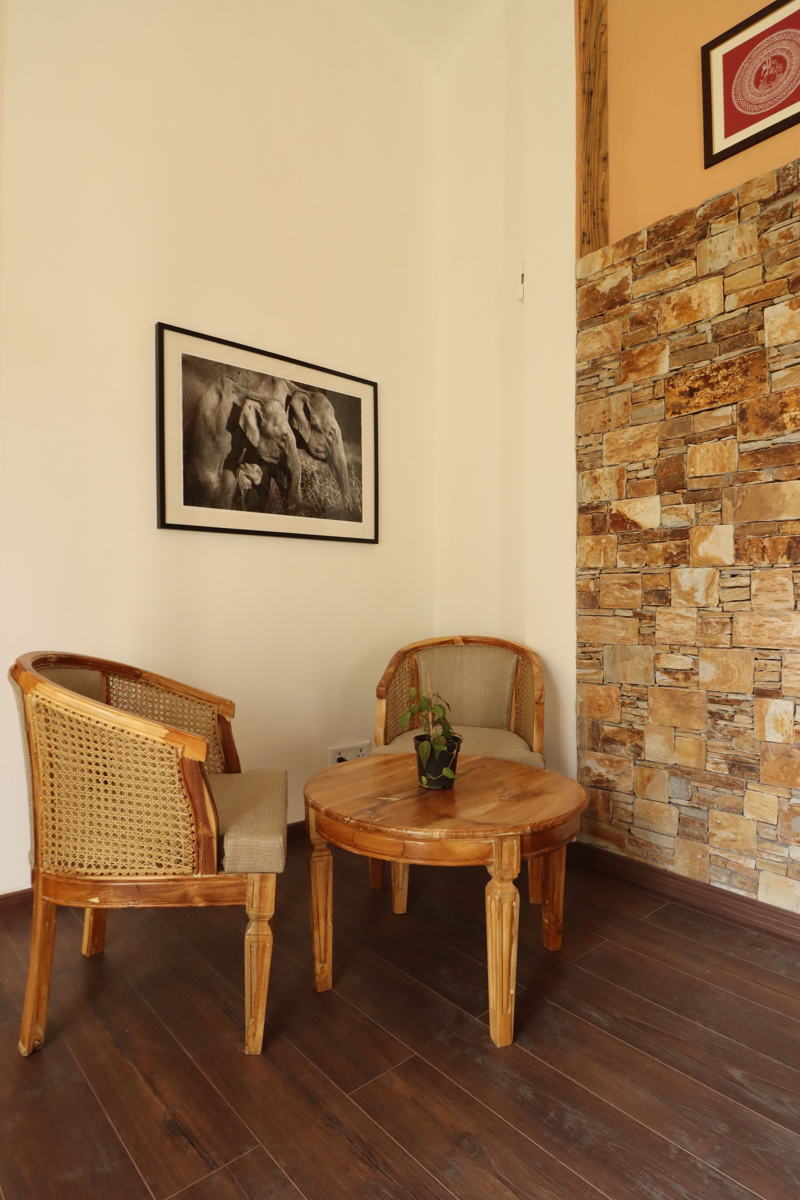A room with two wicker chairs, a round wooden table, and a stone wall.