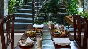 A dining table set with various dishes and a glass of milk, surrounded by chairs, with a staircase and greenery in the background. - Tree of Life Vanvilas Riveredge (Ramnagar)