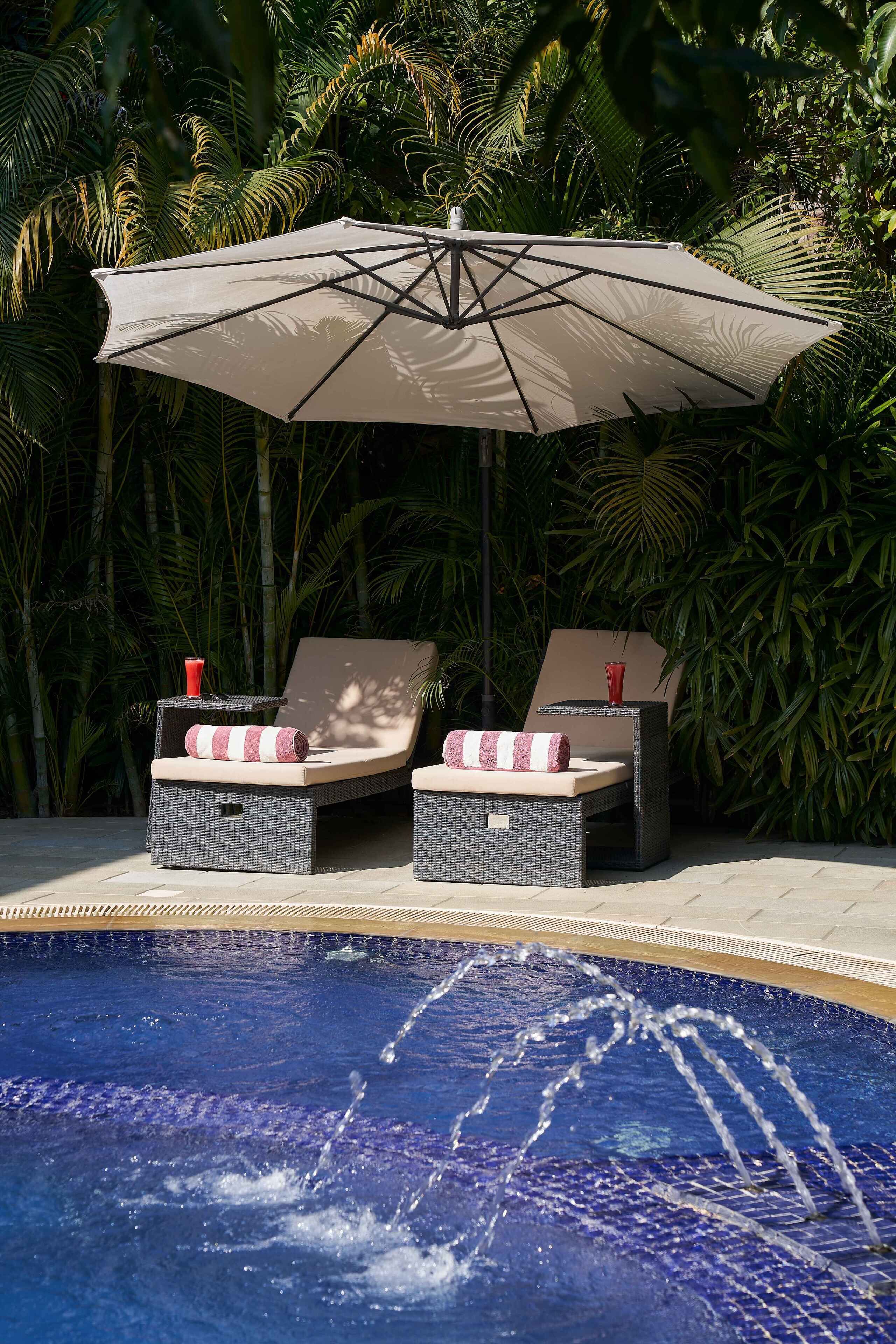 A poolside area with two wicker lounge chairs, a table, and an umbrella.