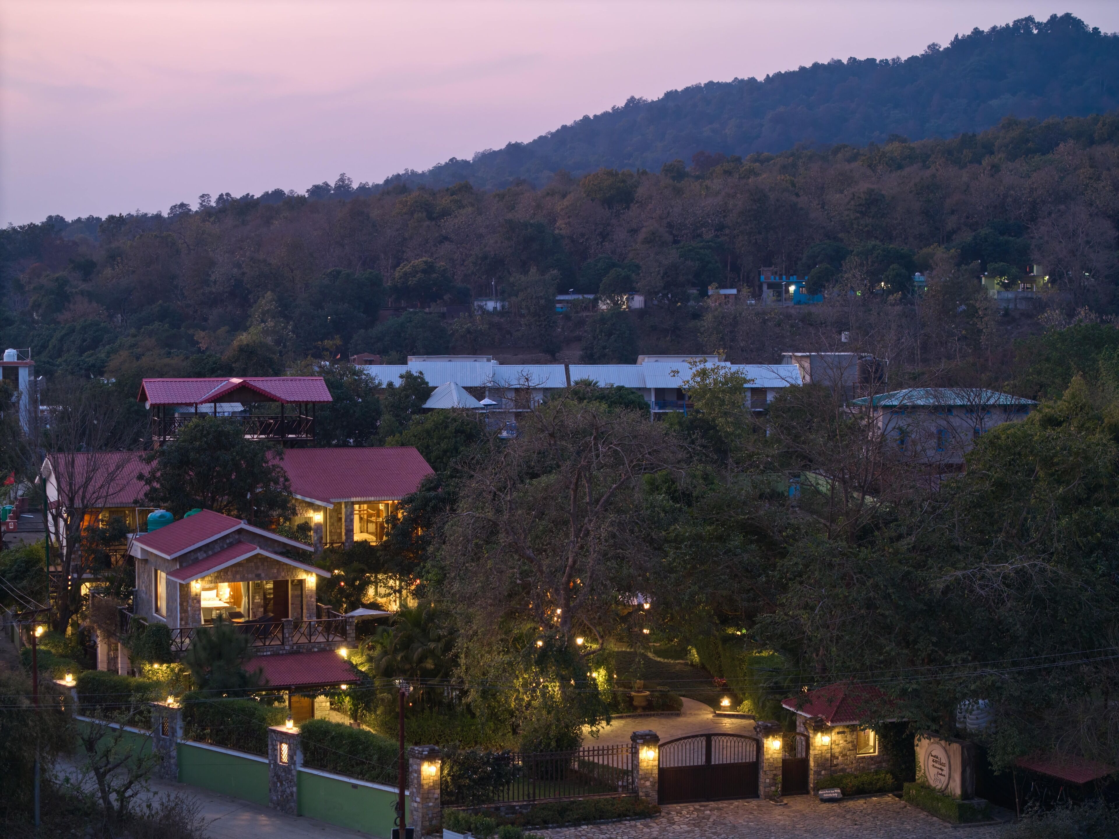 A hillside residential area with houses, a gated entrance, and a stone pathway leading to a building.