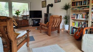 Una sala de estar con un sofá y una silla de madera, una estantería, un televisor y una guitarra.