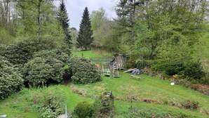 Un jardín con un parque infantil, un cobertizo de madera y diversas plantas.