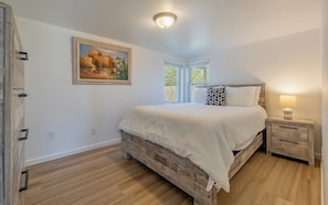 Um quarto com uma cama, uma mesa de cabeceira, um quadro e uma janela.