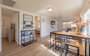 Cozinha moderna com mesa de madeira, banquetas e estante embutida com plantas.