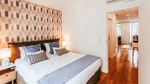 Ein ordentlich bezogenes Bett mit Kopfteil, zwei Nachttischlampen und einer Wand mit Muster.