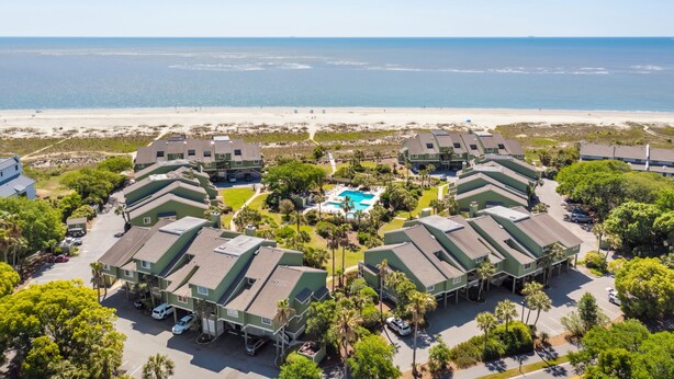 A beachfront hotel with multiple green-roofed buildings, a central swimming pool, and a view of the ocean.
