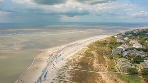 An aerial view of a beach with a row of beach umbrellas and a residential area with houses and a road.