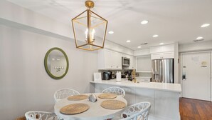 A modern kitchen with white cabinetry, a central island, and a dining area with white chairs and woven placemats.