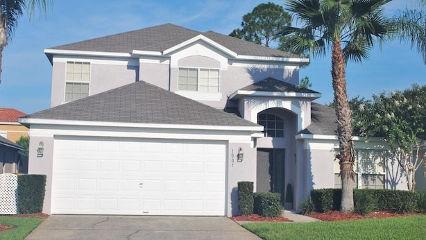 A two-story house with a white garage door, a covered front porch, and a palm tree in the yard. - Ref 502. Lake Berkley. Stunning Villa, own pool. Near Disney (Kissimmee)