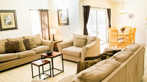 A living room with a sofa, armchair, and a small table. There is a dining table with chairs in the background. - Ref 502. Lake Berkley. Stunning Villa, own pool. Near Disney (Kissimmee)