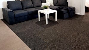 A modern living room with a dark grey sectional sofa, a white coffee table, and a hanging plant. - The Sandbar (Lake Conjola)