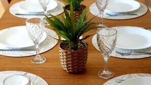 A dining table set with white plates, clear glassware, and a central woven basket containing a green plant. - The Sandbar (Lake Conjola)