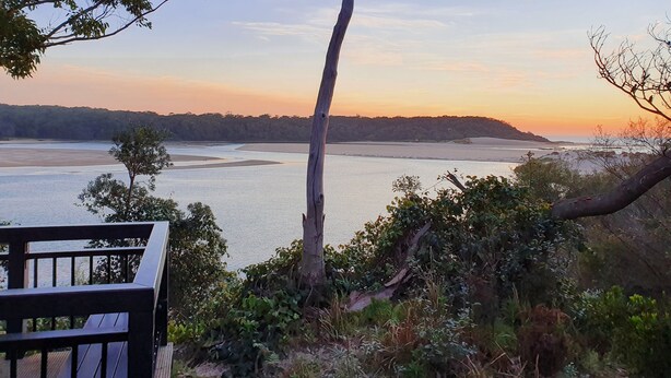 A bench overlooking a coastal landscape with a view of the sea and a tree in the foreground. - The Sandbar (Lake Conjola)