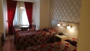 Une chambre d’hôtel avec deux lits, une petite table, une chaise et un bureau avec une lampe.
