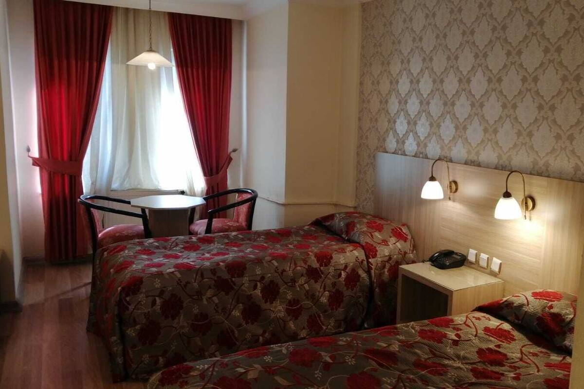 Une chambre d’hôtel avec deux lits, une petite table, une chaise et un bureau avec une lampe.