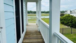 A covered porch with a view of a grassy area and a body of water. - Experience coastal charm at No Egrets, a spacious 3-bedroom retreat in Holden Beach. (Holden Beach)