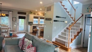 A spacious living room with a grey sofa, wooden staircase, and a kitchen in the background. - Experience coastal charm at No Egrets, a spacious 3-bedroom retreat in Holden Beach. (Holden Beach)