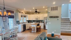 A spacious kitchen with white cabinets, a central island, and a dining area with a wooden table and chairs. - Experience coastal charm at No Egrets, a spacious 3-bedroom retreat in Holden Beach. (Holden Beach)
