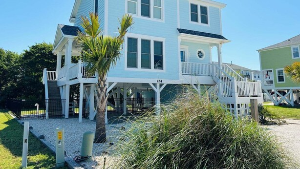 A two-story house with a balcony, a small porch, and a staircase leading to the upper level. - Experience coastal charm at No Egrets, a spacious 3-bedroom retreat in Holden Beach. (Holden Beach)