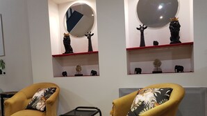 A living room with two yellow armchairs, a small black table, and two wall-mounted shelves with decorative items.