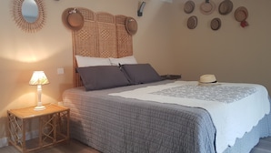 A bedroom with a bed, a bedside table with a lamp, a woven headboard, and several hats on the wall.