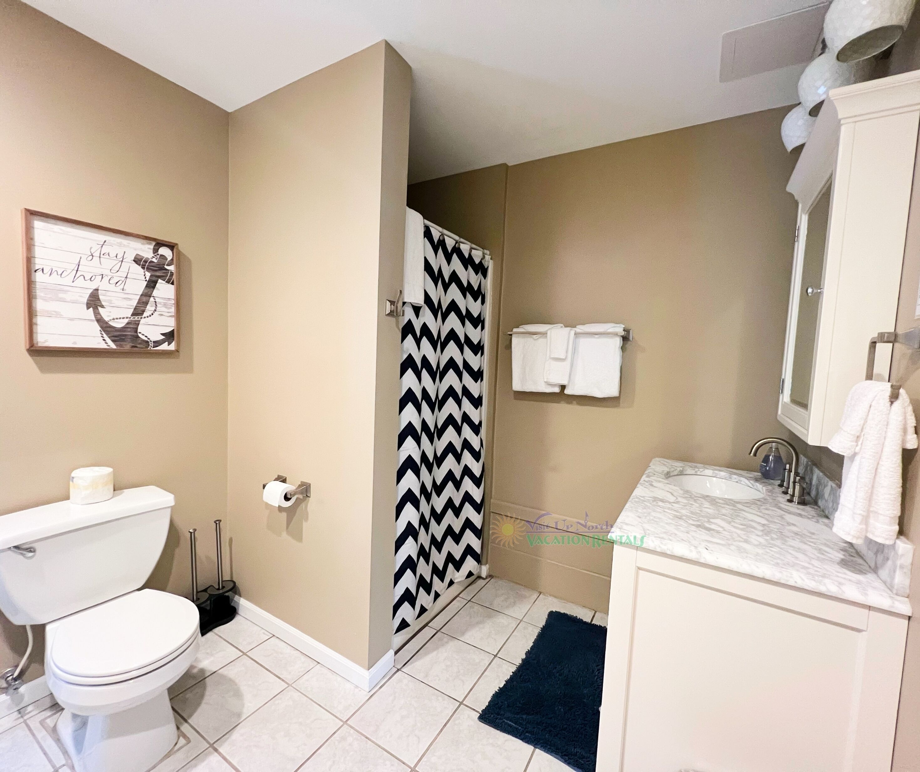 A bathroom with a toilet, sink, and shower. There is a towel rack above the sink and a towel hanging on it.