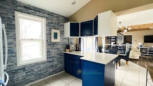 A modern kitchen with blue cabinets, a large island, and a stone backsplash. - Waterfront home on Perch Lake outside Traverse City. Hot tub. Pool table. (South Boardman)