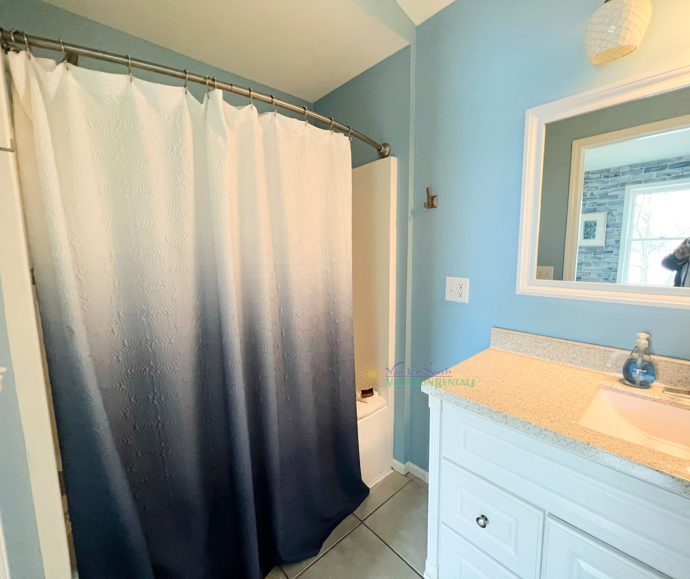A bathroom with a shower curtain, a sink, and a mirror.