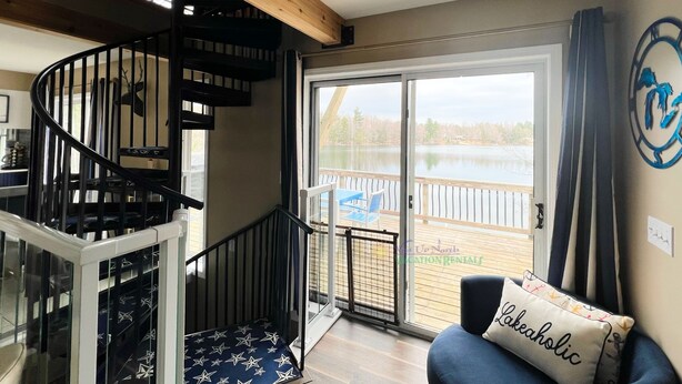 A room with a spiral staircase, a view of a lake, and a couch with a pillow labeled "Lakeaholic". - Waterfront home on Perch Lake outside Traverse City. Hot tub. Pool table. (South Boardman)