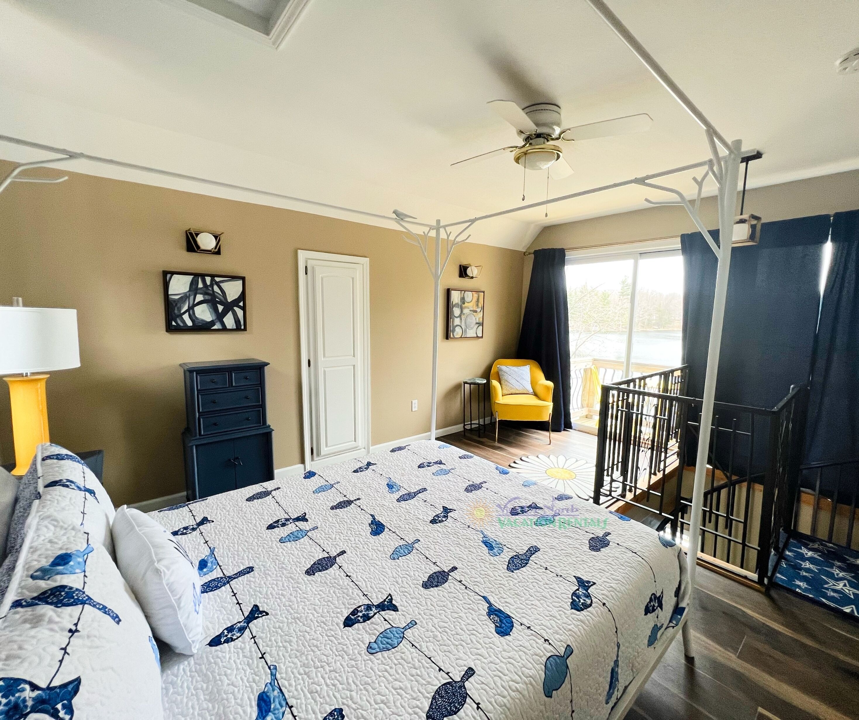 A bedroom with a bed, a nightstand, a dresser, a chair, a balcony, and a ceiling fan.